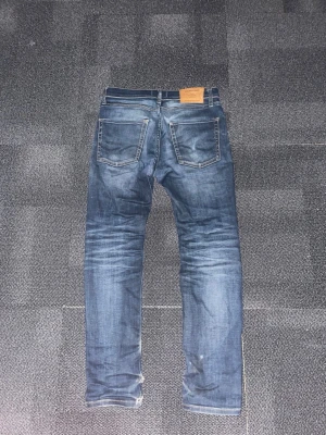 Blå slim fit jeans från Jack and jones - Säljer ett par blå slim fit jeans från Jack and jones med klassisk femficksmodell och snygga slitningar. Jeansen har en skön tvättad look, kontrastsömmar och patch i läder bak i midjan. Perfekta för en avslappnad och trendig stil. W29 men passar 30. Pris går att diskutera.