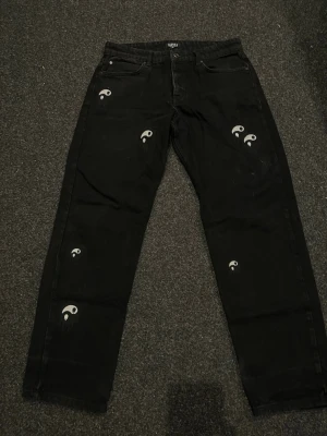 Svarta jeans från boohooMAN - Säljer ett par svarta jeans från boohooMAN med unika tryck på framsidan. Jeansen har rak passform, klassisk femficksdesign och är tillverkade i denim. 