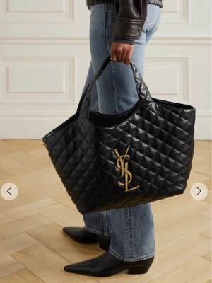 Svart väska YSL - Stilren svart väska från Saint Laurent i quiltat läder med stort YSL-monogram i guld framtill. Väskan har två handtag och rymlig insida, perfekt för att bära allt du behöver. Klassisk design som ger en lyxig touch till din outfit. Pris kan diskuteras.