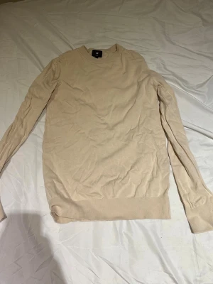 Beige stickad tröja från H&M - Säljer en beige stickad tröja från H&M i slim fit-modell. Tröjan har rund halsringning, långa ärmar och ribbade muddar vid ärmslut och nederkant. Perfekt basplagg för lager på lager och enkel att matcha med olika stilar.