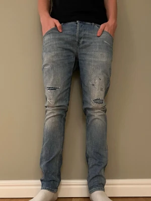 Ljusblå slitna skinny jeans - Säljer ett par ljusblå dondup jeans med slitningar  på framsidan. Jeansen har klassisk femficksmodell och är tillverkade i denim med stretch för skön passform. Perfekta för en avslappnad och trendig look.