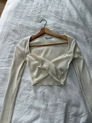 Ribbad omlottopp från Zara - Trendig ribbad omlottopp från Zara i ljus beige färg. Toppen har lång ärm, croppad passform och en snygg omlottdetalj framtill. Perfekt för dig som gillar stilrena och moderna plagg med en twist.