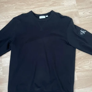 Svart långärmad topp Calvin Klein - Svart långärmad topp från Calvin Klein Jeans med rund halsringning och diskret logga på ärmen. Klassisk och enkel design i mjukt material som passar till det mesta. Perfekt för dig som gillar stilrena plagg med en modern touch.
