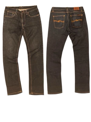 Nudie Leand Dean 32/31 - Säljer ett par mörkblå jeans från Nudie Jeans med klassisk femficksmodell och kontrastsömmar. Jeansen har raka ben och detaljerade bakfickor med Nudie Jeans signaturbrodyr. Materialet är kraftig denim i bomull.