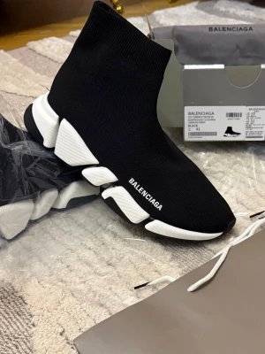 Balenciaga Speed Trainer svarta sneakers - Ikoniska Balenciaga Speed Trainer sneakers i svart stretchig knit med vit chunky sula. Strumpmodell med Balenciaga-logga på sidan och futuristisk design. Perfekta för dig som vill ha en clean och modern look.