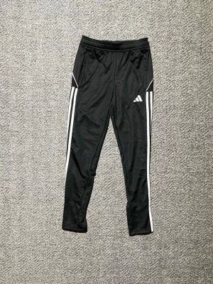 Svarta Adidas träningsbyxor - Hej! Säljer dessa Svarta träningsbyxor från Adidas med vita ränder längs sidorna och Adidas-logga på låret. Storlek 152 men passar bättre om man är lite längre. Byxorna är helt nya men prislappen är inte kvar, eftersom de var för små men glömde lämna tillbaka dem. Köpta för 500kr på Adidas hemsida. Flera bilder finns. Bara att höra av sig vid intresse!!