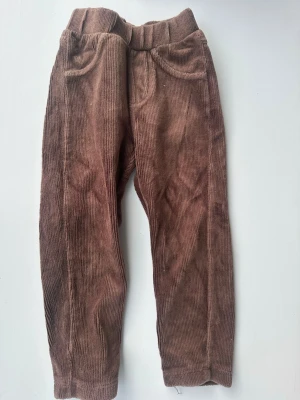 Bruna manchesterbyxor med resår - Säljer ett par bruna manchesterbyxor med resår i midjan och raka ben. Byxorna har två fickor fram och är gjorda i mjuk, bredspårig manchester som ger en retrovibe. Perfekta för dig som gillar avslappnad och trendig stil.