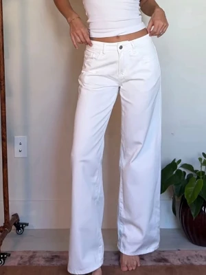 Vita vida jeans med hög midja - Säljer ett par vita jeans med hög midja och raka, vida ben. Jeansen har klassisk femficksdesign och stängs med knapp och dragkedja. Perfekta för en clean och fräsch look. Materialet ser ut att vara bomull eller bomullsblandning.