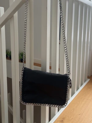 Svart axelväska med kedja - snygg och rymlig väska ifrån tiamo! silvrig kedja och skinn liknande material. enda defekten på väskan är att en ”metallknapp” har gått av men det är inget som syns när den är stängd! 