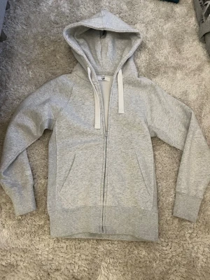 Oanvänd russsemerch zip hoodie - Ljusgrå hoodie med dragkedja från russemerch Klassisk modell med stor huva, vita breda dragsnören och två fickor framtill. Tillverkad i mjukt sweatshirtmaterial, perfekt för en avslappnad stil. Helt oanvänd, pris är ej satt! Kom gärna med bud. 🙌 