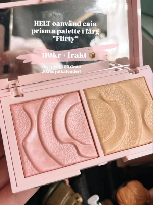 Caia Prisma Palette Flirty highlighter - Caia Prisma Palette i färgen Flirty med två highlighters i rosa och guld. Paletten har ett vågigt mönster i pressat puder och kommer i en ljusrosa förpackning med spegel. Perfekt för att ge glow till ansiktet.