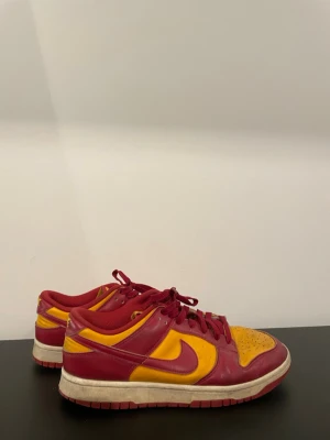 Nike Dunk Low röd/gul sneakers - Nike Dunk Low sneakers i rött och gult med klassisk Swoosh på sidan. Skorna har lågt skaft, röda snören och en vit sula med röda detaljer. 