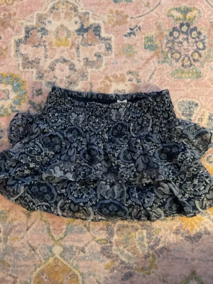 Blå volangkjol från Lindex - Supersöt kort volangkjol från Lindex med blått och grått blommönster. Kjolen har bred resår i midjan👩‍❤️‍💋‍👩❤️👸🏼