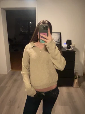 Beige stickad tröja med krage - Mysig beige stickad tröja med avslappnad passform och krage. Tröjan har långa ärmar och ribbade muddar vid ärmslut och nederkant. 