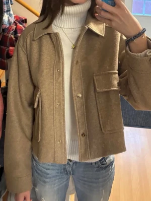 Beige ullcardigan med fickor - Snygg beige cardiganjacka i ullmix med stora fickor framtill och knappar. Jackan har en avslappnad passform, klassisk krage och är perfekt att slänga över en polotröja. Passar till jeans för en chill look. Säljer då den är fel färg på mig.