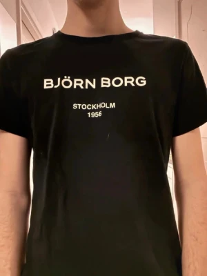 Björn Borg t-shirt - Snygg t-shirt från Björn Borg med vit text på bröstet där det står 'BJÖRN BORG STOCKHOLM 1956'. Klassisk passform och rund hals. Perfekt till jeans eller shorts för en clean och enkel stil.