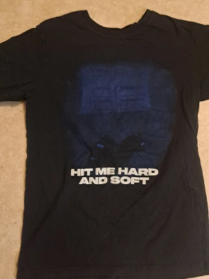 Svart t-shirt med tryck 'Hit Me Hard And Soft' av billie eilish - Cool svart t-shirt med ett blått tryck och texten 'HIT ME HARD AND SOFT' på framsidan. Klassisk rund hals och korta ärmar. Perfekt för dig som gillar statement-plagg och vill sticka ut lite extra. Av billie elish 1 HOODIE FÖR 250!! OBS!!! RÖD HOODIE ÄR DET LITE FLEKAR PÅ TAR FÖR 150 PÅ DEN!! VITA TRÖJAN FÖR 100-150!! OBS!!!!! DJUR FINNS I HEMMET