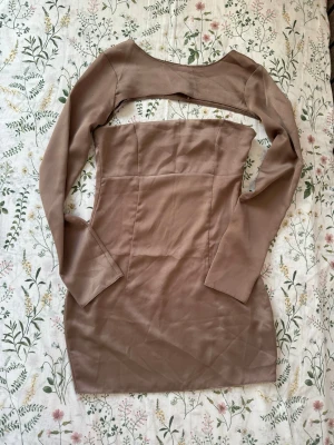 Beige kort klänning med ärmar - Trendig beige kortklänning med avtagbara långa ärmar. Klänningen är axelbandslös och har en figurnära passform som framhäver siluetten. Perfekt för dig som vill ha en stilren och modern look. Materialet känns mjukt och följsamt.