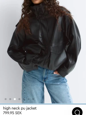 Svart skinnjacka med hög krage - Snygg slutsåld svart skinnjacka i oversized modell med hög krage och dragkedja framtill. Jackan har stora fickor med lock och knapp, samt ribbade muddar vid ärmslut och nederkant. Köpt för 800