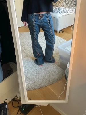 Coola jeans med snörning  - Unika blå jeans med snygg snörning längs hela framsidan och vid midjan. Modellen är lågmidjad och har raka ben med en utsvengling längst nertill med normal passform. Jeansen är tillverkade i stretch denim och har bakfickor. 