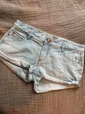 Ljusblå lågmidjade jeansshorts från Gina Tricot - Säljer ett par ljusblå denimshorts från Gina Tricot med låg midja. Shortsen har normal passform och stängs med knapp och dragkedja. Perfekta till sommaren och lätta att matcha med olika toppar. Mått finns på bilderna. 
