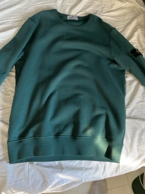 Grön sweatshirt från Stone Island - Snygg grön sweatshirt från Stone Island med klassisk rund halsringning och ikonisk logga på ärmen. Tröjan är tillverkad i mjuk bomull och har ribbade muddar vid ärmslut och nederkant. Perfekt för en avslappnad och trendig stil.
