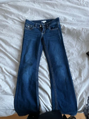 Blå low bootcut jeans - Säljer ett par mörkblå bootcut jeans från Gina Tricot med vita kontrastsömmar och klassisk femficksmodell. Jeansen har låg midja. Säljer för att de inte passa längre