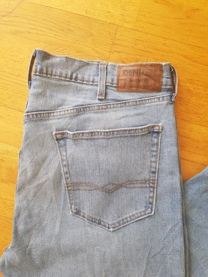 Blå jeans från Denizen Levi's - Säljer ett par klassiska blå jeans från Denizen by Levi's. Jeansen har raka ben, fem fickor och snygga kontrastsömmar. Tillverkade i mjuk denim med en skön passform och läderpatch bak i midjan.
