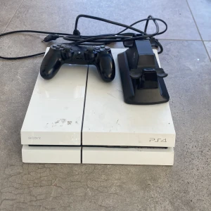  PS4 med kontroll och laddarstativ - Säljer en vit PlayStation 4 från Sony med en svart DualShock 4-handkontroll och ett laddarstativ från Piranha. Strömkabel och HDMI kabel kommer med. Hör av er vid frågor