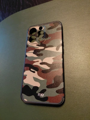 Camo skal till iPhone 13 Pro från NXE - Snyggt kamouflagemönstrat mobilskal till iPhone 13 Pro från NXE. Skalet har en matt finish och är gjort i tåligt plastmaterial. Perfekt för dig som vill ha en cool och unik look på mobilen. Färgerna går i grönt, svart, beige och brunt.