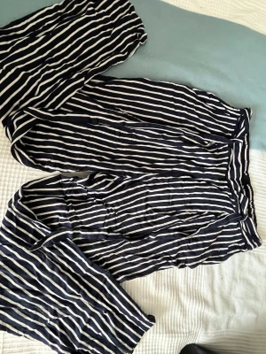 Randiga linnebyxor från Monki - Säljer ett par snygga linnebyxor från Monki i storlek 36. Byxorna är marinblå med vita vertikala ränder och har en avslappnad passform med resår i midjan. Perfekta för en chill och trendig look i sommar.