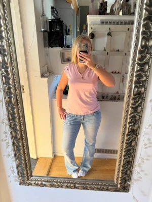 Ljusrosa topp med spetsärmar - Supersöt ljusrosa topp med v-ringning och korta spetsärmar. Toppen har en enkel, rak passform och är gjord i mjuk bomull. Spetsdetaljerna på ärmarna ger en romantisk vibe och gör den extra fin till både jeans och kjol.