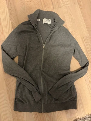 Grå ziptröja från Selected Homme - Snygg grå ziptröja från Selected Homme med hög krage och hel dragkedja framtill. Tröjan har långa ärmar och ribbade muddar vid ärmslut och nederkant. Perfekt att slänga på sig över en t-shirt för en avslappnad look.