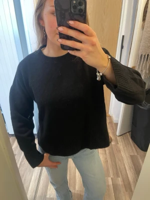 Svart stickad tröja i relaxed fit - En svart stickad tröja med rund halsringning och avslappnad passform. Tröjan har långa ärmar och ribbade muddar vid ärmslut och nederkant. Perfekt för lager på lager och enkel att matcha med jeans eller kjol.