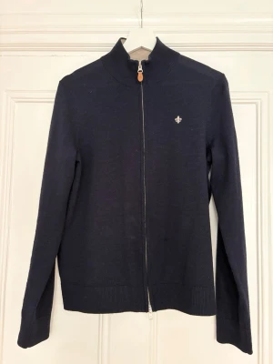 Marinblå ziptröja från Morris - Snygg marinblå ziptröja från Morris i 100% merinoull. Tröjan har hög krage, hel dragkedja framtill och en liten broderad logga på bröstet. Perfekt för lager på lager och stilrena outfits.