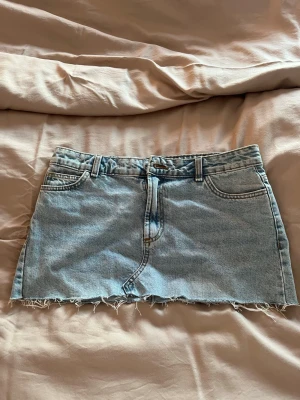 Ljusblå jeanskjol från Primark - Trendig ljusblå jeanskjol från Primark med rå kant nertill och klassiska fem fickor. Kjolen har dragkedja framtill. Perfekt för dig som gillar en avslappnad och cool stil. Säljer på grund av att den är för stor på mig.