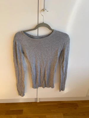 Grå långärmad topp i bomull - En enkel och stilren grå långärmad topp med rund halsringning. Tillverkad i mjuk bomull och har en normal passform som funkar till det mesta. Perfekt basplagg att ha i garderoben. Har sytt in midjan lite så skulle nog vela säga att det är en XS nu men det står M 