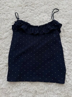 Mörkblå prickig linnetopp Mango - Supersöt mörkblå linnetopp från Mango med små vita prickar och volangdetalj upptill. Tunna axelband och luftig passform gör den perfekt för varma dagar. Enkel att styla med jeans eller kjol för en chill look.