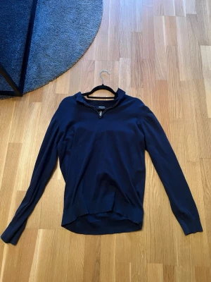 Mörkblå ziptröja från Indicode - Mörkblå långärmad tröja från Indicode med halv dragkedja framtill och ribbad krage. Tröjan har en enkel, stilren design och är tillverkad i ett mjukt material som passar perfekt till vardagslooken.