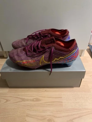 Nike Mercurial  fotbollsskor - Säljer ett par Nike Mercurial fotbollsskor i lila och vinrött med färgglada detaljer i gult, blått och rött. Skorna har snörning, vapor modell  och är tillverkade i ett lätt syntetmaterial för bästa bollkontroll. Säljer för dem är för små. Pris går att diskutera. Skorna kommer med box och påse 