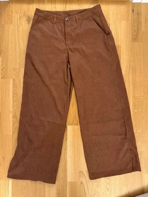 Bruna vida manchesterbyxor - Säljer ett par bruna manchesterbyxor med raka, vida ben och klassisk passform. Byxorna har fickor fram, bälteshällor och stängs med knapp och dragkedja. Perfekta för dig som gillar retrostil och mjukt material.