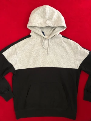 Svart och grå hoodie med huva - Snygg hoodie i svart och ljusgrått med klassisk huva och dragsnören. Hoodien har en stor magficka och ribbade muddar vid ärmslut och nederkant. Perfekt för en avslappnad streetwear-look. Tillverkad i mjuk bomullsblandning.