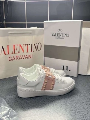 Valentino Rockstud rosa sneakers - Snygga vita sneakers från Valentino Garavani med ljusrosa band och ikoniska nitar över vristen. Alla storlekar finns 35-39