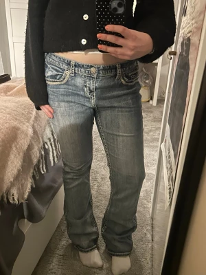 Blå bootcut jeans med broderi - Säljer ett par blå low-waist bootcut jeans med snygga vita broderier på fickorna och slitna detaljer. Jeansen är köpta på plick och står inget märke i. 💖💖💖
