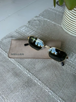 Guldiga hexagonala solglasögon - Snygga solglasögon från Meller med tunn guldfärgad metallbåge och mörkgröna/ svarta glas. Klassisk och trendig design som passar till alla outfits. Skalmarna har svarta detaljer i ändarna för extra komfort. Helt oanvända, fodral och putsduk medföljer