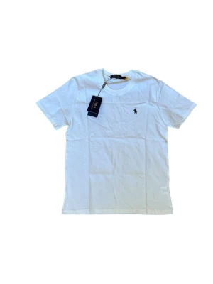 Vit t-shirt från Polo Ralph Lauren - Klassisk vit t-shirt från Polo Ralph Lauren med liten broderad logga på bröstet. T-shirten har rund halsringning och korta ärmar. Tillverkad i mjuk bomull för en skön känsla och enkel stil.