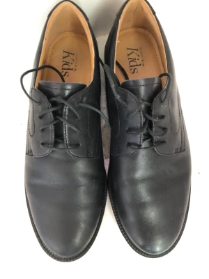 Svarta loafers från Skys - Säljer ett par klassiska svarta loafers från Skys. Skorna är i slätt läder med rundad tå och har en enkel, stilren design. Insidan är ljusbrun och de har snörning framtill för en snygg look. Perfekta för dig som gillar tidlös stil.