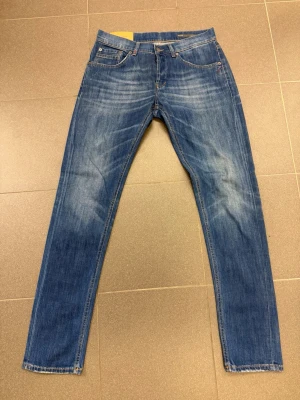 Dondup Slim fit jeans  - Säljer ett par klassiska blå jeans med raka ben och snygga slitningar framtill och baktill från Dondup. Jeansen har fem fickor, orangea sömmar och knappgylf. Materialet är denim i bomull och passformen är normal. Perfekta för en avslappnad och trendig look.
