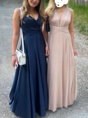 Marinblå långklänning JJ's House - Säljer min balklänning i väldigt fint skick, endast använd en gång! Elegant marinblå långklänning från JJ's House med v-ringad omlottdesign, smala axelband och hög slits. Klänningen har ett glansigt tyg som ger en lyxig känsla och ett svepande fall. Perfekt för bal eller festliga tillfällen. 