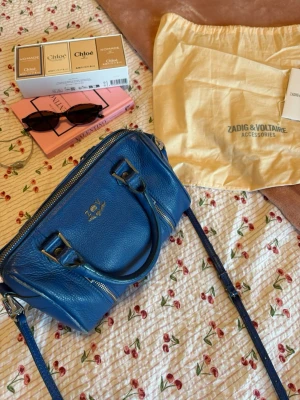 Blå Zadig & Voltaire handväska - Snygg blå handväska från Zadig & Voltaire i kraftigt läder och logga framtill. Väskan har både handtag och axelrem samt två dragkedjor framtill för extra stilpoäng. Perfekt för dig som vill ha en trendig och rymlig väska. Skriv om du har frågor, finns fler bilder på min vinted Daisy08080808